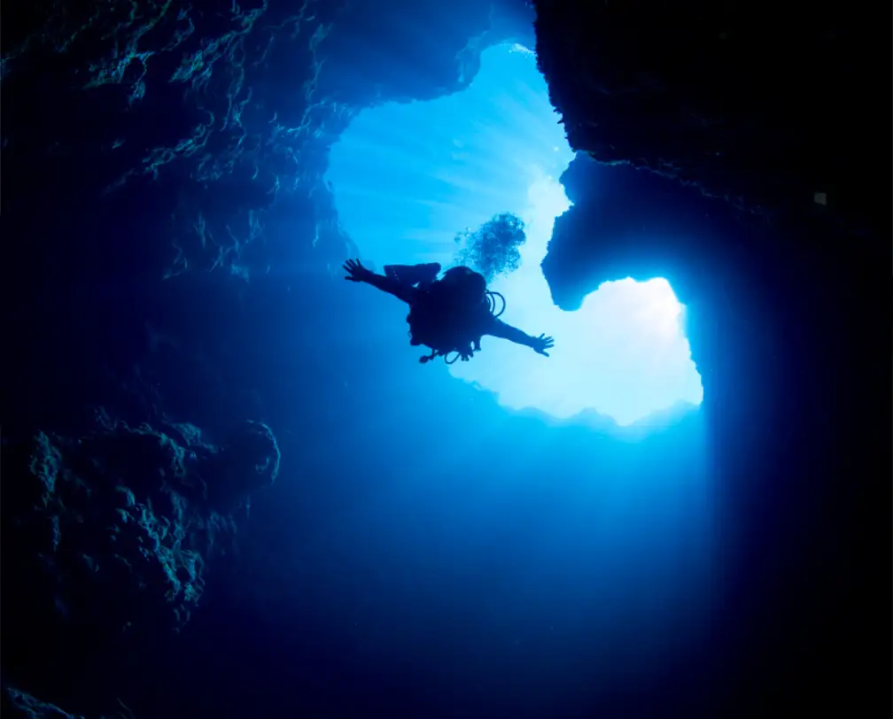 Diver submerging into the Blue Holes in Palau, the sun in the background he dives into the dark cave